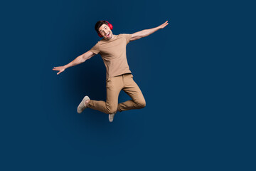 Full size photo of childish carefree man dressed beige t-shirt flying playing hold arms like wings isolated on dark blue color background