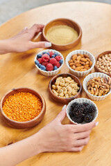 cropped woman with ripe fresh blackberries near nuts and berries with legumes, vegetarianism concept