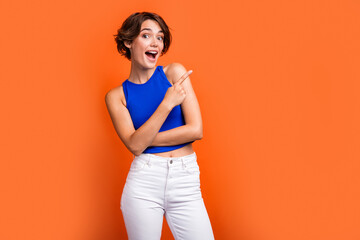 Photo of cheerful impressed girl dressed blue top pointing finger empty space open mouth isolated orange color background