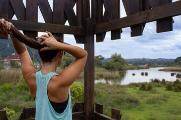 Young woman doing a ponytail after a run or a walk. She is starting to hold her long brown hair...