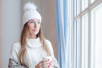 Beautiful winter woman holding hot dring and resting at home, romantic portrait