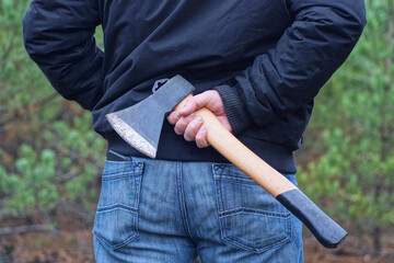 one man in blue black clothes hides his hand with a gray brown ax behind his back on the street