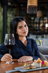 Elegant young Asian woman with glass of red wine sitting by the table in restaurant alone