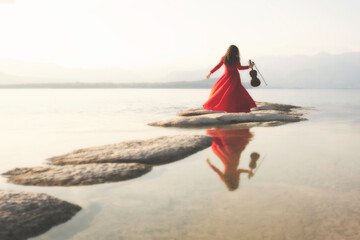 woman in red with violin jumps between a path of stones leading to the sea, abstract concept