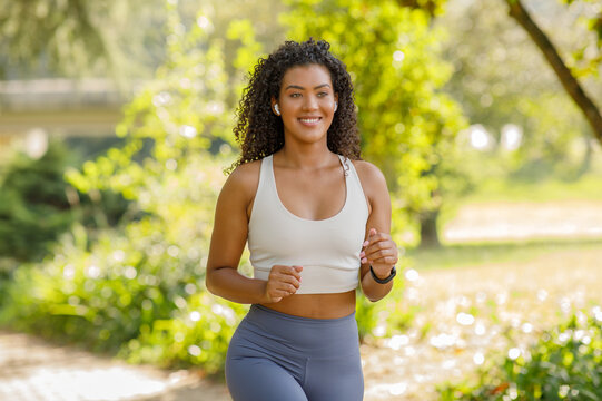Energetic young woman in fitwear running in park with earbuds