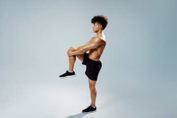 sportsman standing doing knee to chest stretch exercise, gray background - obrazy, fototapety, plakaty