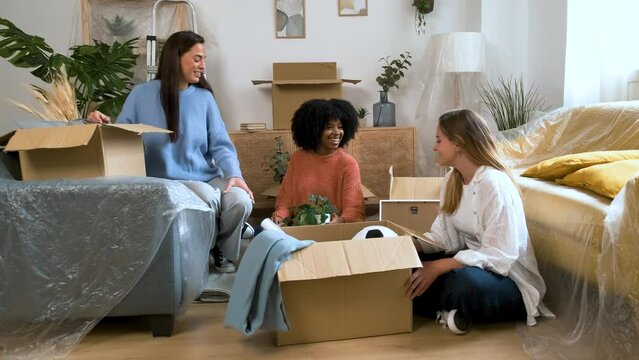 Group of three female happy friends unpacking, moving into student flat. New residence relocation.