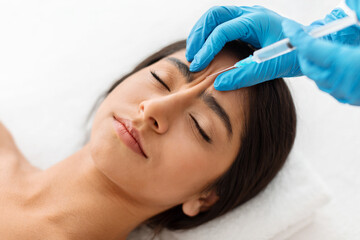 Indian woman getting cosmetic injection between eyebrows at beauty center
