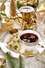 Christmas Eve red borscht with dumplings on festive table in white and gold colors
