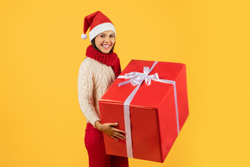 woman in Santa hat cheerfully holding large Christmas present, studio