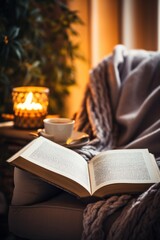  woman sits in a cozy armchair, wrapped in a soft blanket and reading a book by the fire