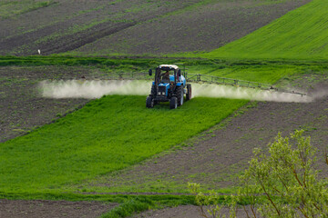 Fototapeta premium Aerial view of tractor spraying crop in green farm fields with pesticide