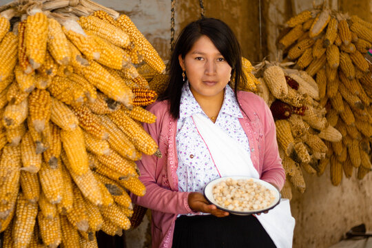 Mujer andina latinoamericana sosteniendo un plato al fondo ma&iacute;z colgados en la casa producci&oacute;n, Cultura, estilo de vida saludable,