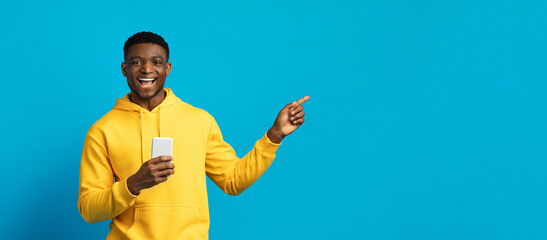 Happy young black guy in yellow hoodie using smartphone, panorama