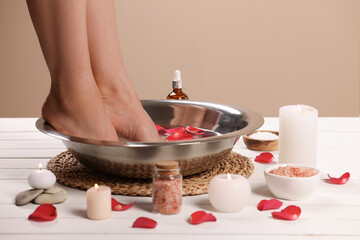 Obraz na płótnie Canvas Woman soaking her feet in bowl with water and rose petals on white wooden surface, closeup. Pedicure procedure