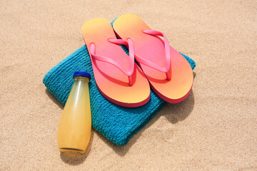 Fototapeta na wymiar Stylish sunglasses, flip flops, towel and bottle of refreshing drink on sand