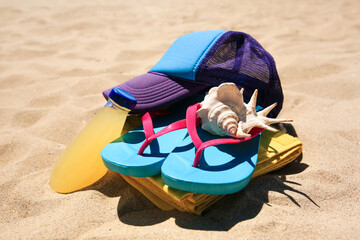 Cap, flip flops, seashell and refreshing drink on beach, closeup