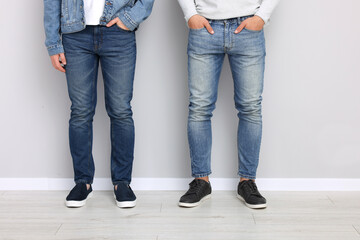 Men in stylish jeans near light grey wall indoors, closeup