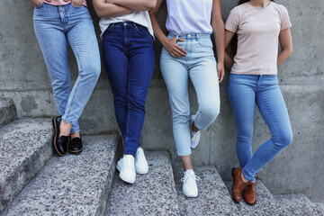 Women in stylish jeans on stairs near stone wall outdoors, closeup