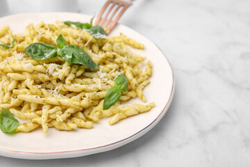 Plate of delicious trofie pasta with pesto sauce, cheese and basil leaves on white marble table, closeup. Space for text