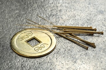 Acupuncture needles and ancient coin on grey textured table, closeup