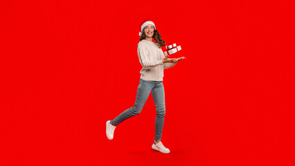 Fototapeta na wymiar woman in Santa hat leaps with gift box, red background