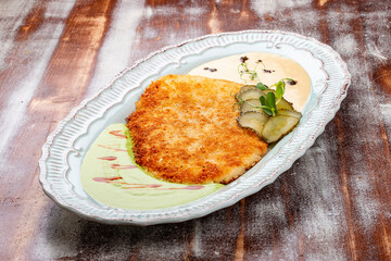 Viennese chicken schnitzel with sauces and pickles. Haute cuisine. On a wooden background.