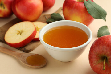 Delicious apples, bowl of honey and spoon on beige background, closeup