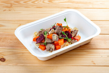Veal loin stewed with carrots and cabbage. Healthy diet. Takeaway food. Ecological packaging. On a wooden background.