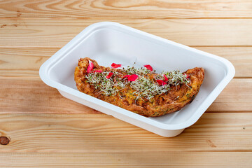 Omelet with mozzarella and tomatoes. Healthy diet. Takeaway food. Eco packaging. On a wooden background.