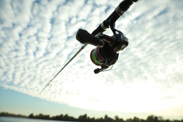 Fishing rod with reel under cloudy sky, low angle view