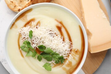 Delicious cream soup with parmesan cheese, soy sauce and parsley in bowl on light grey table, flat lay