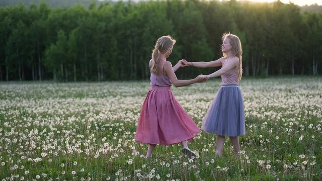 Young and happy girls are spinning and dancing in a meadow full of dandelions.