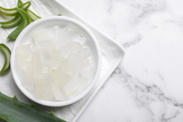 Aloe vera gel and slices of plant on white marble table, top view. Space for text