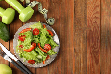 Healthy diet. Salad, cutlery, dumbbells and measuring tape on wooden table, flat lay with space for...