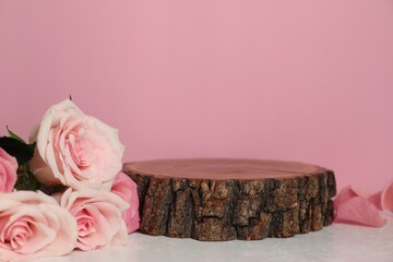 Stylish presentation of product. Beautiful roses and wooden podium on light textured table against pink background, space for text