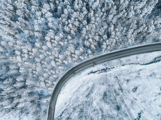 Aerial top view of winter road cars and snow covered forest with frozen lake water
