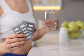 Weight loss. Woman with pills and glass of water at table indoors, closeup. Space for text