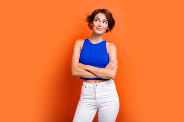 Photo of dreamy adorable girl dressed blue top arms folded looking empty space isolated orange color background
