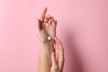 Woman applying cosmetic cream onto hand on pink background, top view