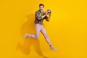 Fototapeta na wymiar Full body photo of ready to party man catching small disco ball during performance concert he jumping isolated on yellow color background