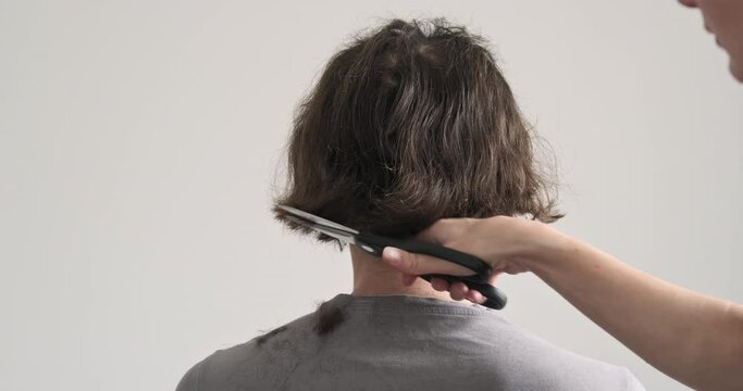 Female barber scissoring male client's hair from behind. Concept of hairdresser work, haircut, long fluffy hair, hairstyle.
