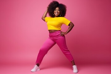 A young pretty African American girl dances in full length against a solid pink background. Happy smiling woman, people emotions concept, joy, laughter, fun