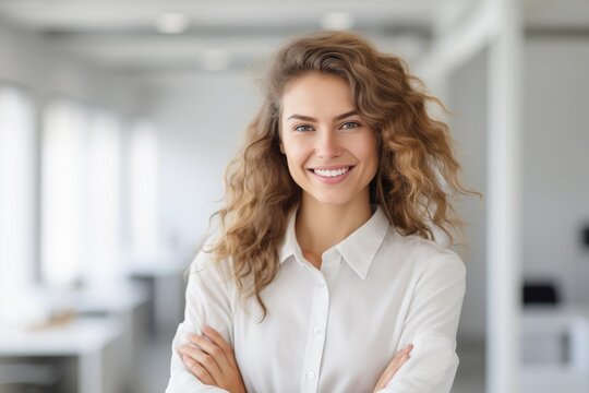 Smiling young woman with blond curly hair in a white blouse in the office, copy space