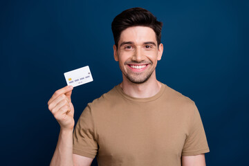 Photo of nice joyful man wear beige trendy clothes hold plastic bank card isolated on dark blue...