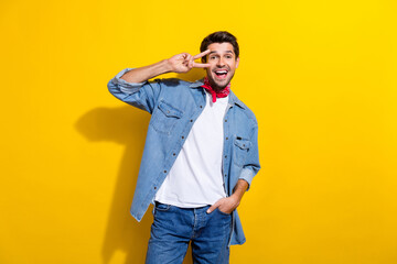 Photo portrait of attractive young man show excited v-sign wear trendy jeans clothes isolated on yellow color background