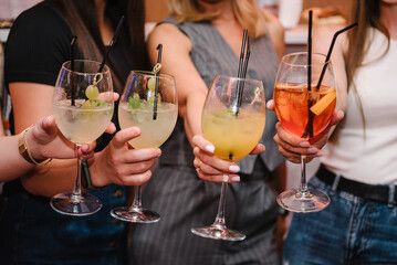 Group of friends partying in nightclub. Happy young people cheering drinks at bar restaurant. Toasting, summer colorful cocktails. Cheers with glasses at pub. Party time concept. Side view of hands up - obrazy, fototapety, plakaty