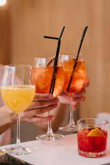 Hands waiter takes alcoholic cocktails with slice orange. Fresh healthy lemon drinks. Ice cold modern gourmet craft four cocktails on bar with blurry restaurant background. Summer refreshing drink.