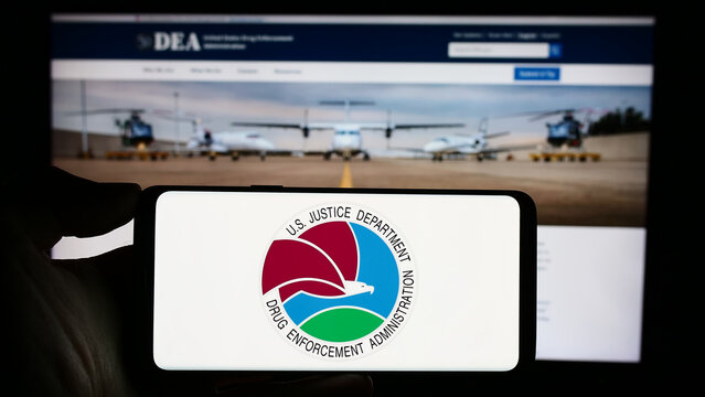 Stuttgart, Germany - 11-11-2023: Person holding cellphone with seal of United States Drug Enforcement Administration (DEA) in front of webpage. Focus on phone display.