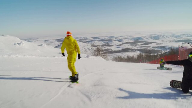A girl in a yellow suit goes down the slope on a snowboard.